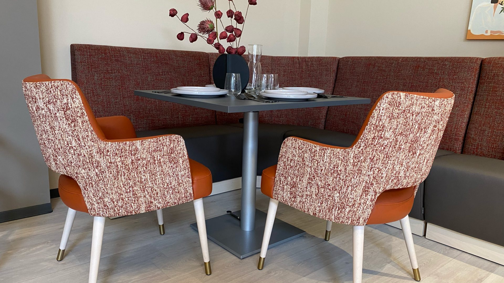 Table à hauteur variable, banquettes et chaises avec accoudoirs dans la salle à manger d'un EHPAD